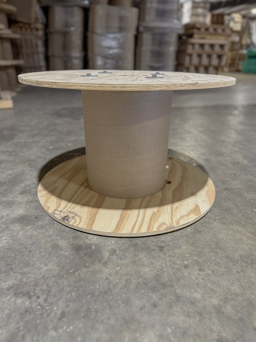 A single cable reel with a cardboard core and plywood flanges on a warehouse floor
